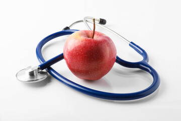 Ripe apple and stethoscope on white table, closeup