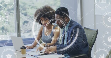 Collaborating woman in sleeveless top and male in suit reviewing papers in office laptop coffee HUD