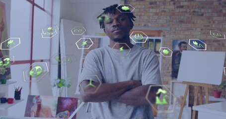 Standing man wearing grey tee, looking toward camera in art studio, easels and green energy icons