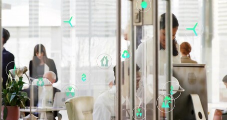 Working team in suits using computers in open-plan office by glass walls, displaying green icons