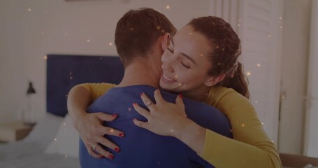 Embracing couple with woman smiling and hugging man in bedroom near bed, showing ring, particles