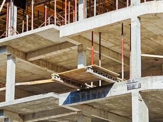 Concrete building under construction with exposed formwork, support beams, and scaffolding showing structural framework of multi-story development project