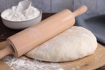 Raw dough, rolling pin and flour on wooden table, closeup