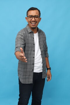 Middle age Asian man smiling looking at camera, handshake gesture, concept of getting acquainted, introducing yourself or congratulating, standing isolated on blue background.