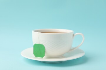Obraz premium Tea brewing. Cup with tea bag on light blue background, closeup