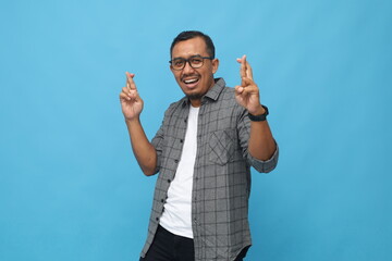 Middle age Asian man smiling in casual clothes, crossing fingers looking at camera, making a wish...