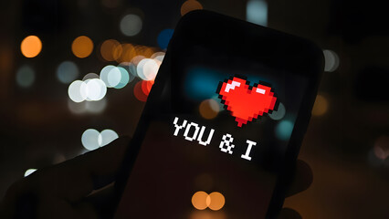 Smartphone screen displaying pixel art red heart and You & I text at night with city bokeh background