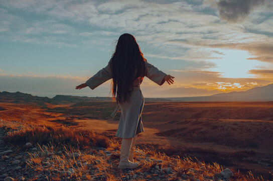 Young beautiful woman standing on sunset in the mountains background