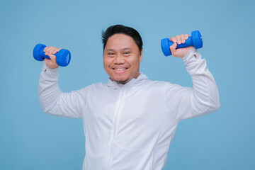 Close up of young Asian man in the gym lifting dumbbell wearing white t-shirt with happy laughing expression on turquoise blue background