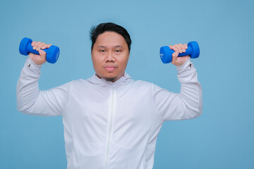 Close up of young Asian man in the gym lifting dumbbell wearing white t-shirt with happy laughing expression on turquoise blue background