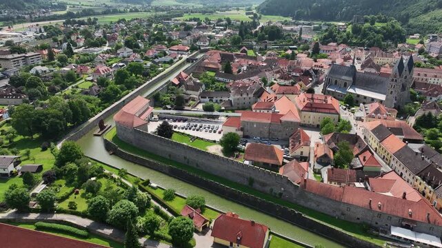 Summer drone footage showing medieval Friesach, old fortified walls, rooftops, towers, hills, serene atmosphere, warm daylight, gentle cinematic motion