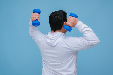 young asian man lifting dumbbells in both hands, seen from behind wearing a white t-shirt on turquoise blue background 