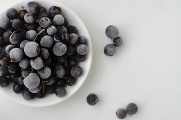 Frozen blackcurrants in white bowl on table.