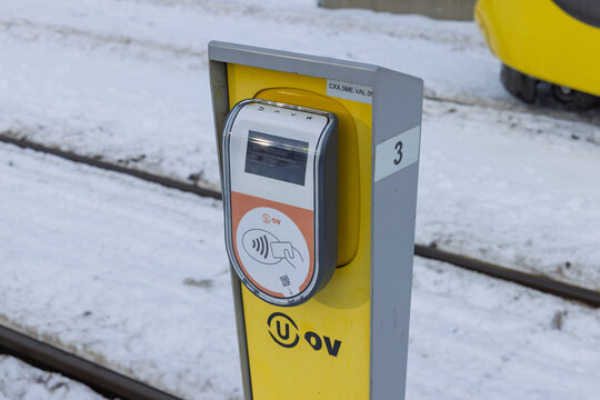 Close-up of a yellow U-OV public transport check-in card reader pole at a tram stop in Utrecht surrounded by white winter snow and ice. Utrecht Netherlands, 6 january 2026
