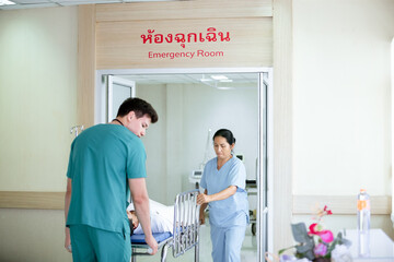 A male doctor in green scrubs and a female nurse in blue scrubs are carefully guiding the stretcher...