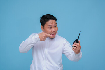 Young Asian man talking on Handy Talkie with very angry expression wearing white t-shirt on turquoise blue backgroun
