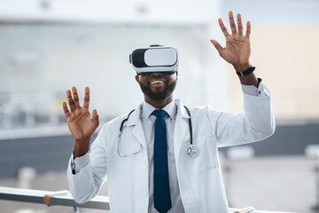 A doctor wears a virtual reality headset and raises both hands in excitement. The setting is a modern medical facility. He appears engaged in a new technology experience.