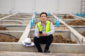 texting on cell phone while relaxing. Civil engineer Asian man in safety hard hat helmet working at construction site