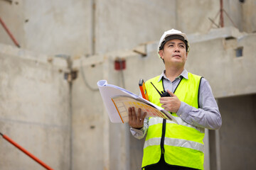 walkie talkie, Asian Man working, Architect or contractor working on house building under construction. Professional Architects Engineer construction site. Civil Engineering in safety harthat helmet