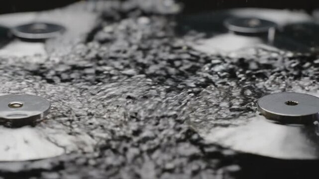 Abstract macro shot of rapidly rising effervescent bubbles surrounding reflective metallic discs spinning on a dark liquid surface generating powerful waves bubbles, hypnotic, rotating