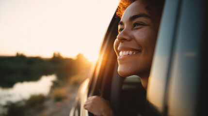 Smiling woman enjoying fresh air while riding in a car at sunset.