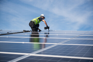 Technician installing solar panels on factory roof for green energy. A skilled technician in safety gear is working on a solar panel installation on rooftop.