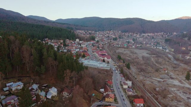 Aerial drone footage of the DN1 road crossing Busteni town, with the Carpathian Mountains surrounding the urban area, filmed during winter daylight in Busteni, Romania.