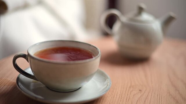 Close up of a ceramic cup filled with hot tea placed on a matching saucer on a wooden table