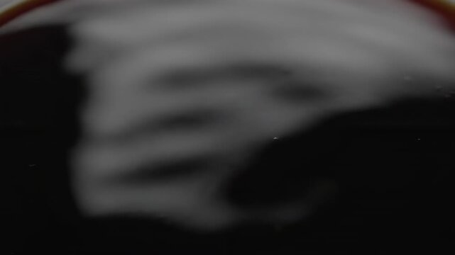 Abstract macro top view seamless loop of the glossy surface of intensely black coffee subtly reflecting ambient light while gently rippling and settling digital display, beverage, modern