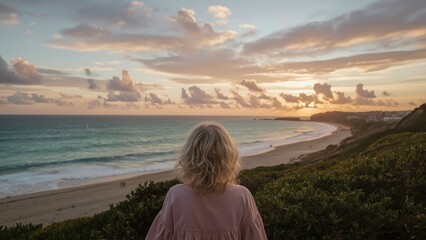Fototapeta premium A woman overlooking the beach at sunset with clouds and ocean view.