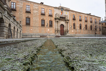 A water installation by Cristina Iglesias featuring sculpted roots and branches in the square of Toledo Cathedral with historic brick buildings behind.