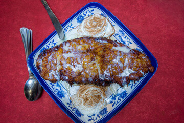 A plate of Spanish Torrijas dessert topped with cream and cinnamon on a red tablecloth in Toledo Spain.
