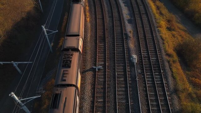 Aerial view of a modern train traveling on multiple railway tracks through autumn foliage drone