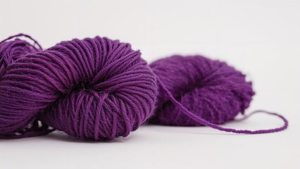 Purple yarn ball with loose strand on a white background. Craft and knitting, textile material concept. Yarn and knitting supplies. The concept of knitting and fabric creation.