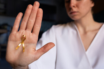 A doctor holds a gold ribbon in their palm, symbolizing support for childhood cancer awareness on...