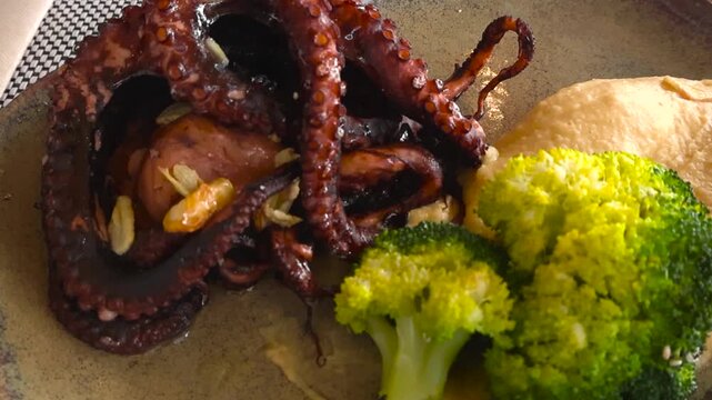 Close-up of perfectly grilled octopus with char marks, broccoli and sweet potato mash in a Portuguese restaurant, camera gliding over a colorful healthy seafood dish