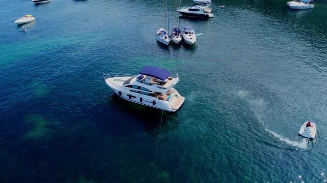 Aerial view of a luxury motor yacht anchored in clear blue water with a small dinghy boat moving nearby in Malta.