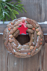 Kranz aus Fichtenzapfen, Walnüssen und Haselnüssen hängend auf einer Holztür