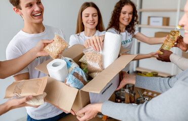 Young male and female volunteers happily pack food and personal hygiene products into boxes for donation. This charitable activity promotes community support and generosity among millennials.