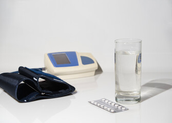 On white glass are pills and a glass of water against the background of a tonometer, with a shadow and space for text.