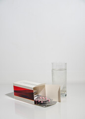 Blister pack of pink tablets and a glass of water, on white glass, space for text.
