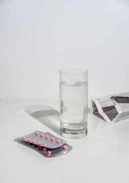 Blister pack of pink tablets, paper instructions and a glass of water on a white background, space for text.