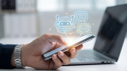 Person using smartphone to interact with chatbot, showcasing technology and communication. scene conveys modern business environment with laptop in background