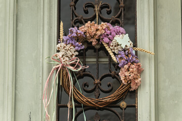   
Decorative wreath on a door in Patmos, Greece, crafted from intertwined twigs and adorned with dried flowers in soft pink, purple, and white hues. 