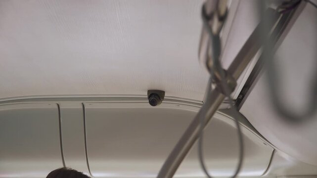 Surveillance camera mounted on ceiling in interior of public transport. Monitoring order and recording violations in bus. Compliance with rules of conduct during transportation of passengers.