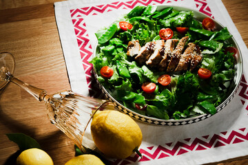 mediterranean styled salad with green lettuce leaves, peas, grilled chicken meat, cherry tomatoes, dressed with olive oil, served for one