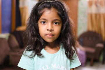 Child with long hair in indoor setting focusing on camera