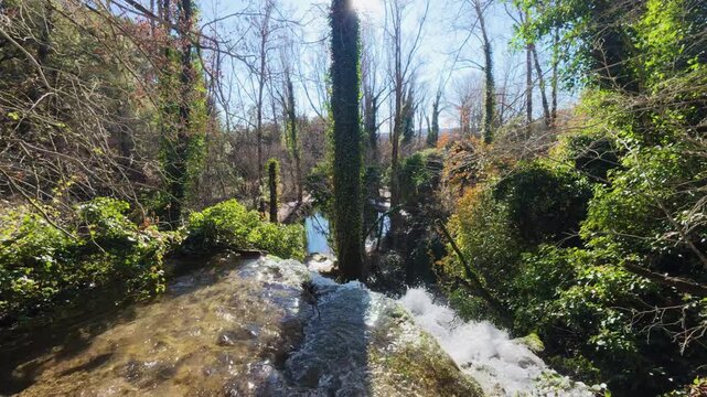 A person enjoys a peaceful winter walk on a trail near the stunning Fuentetoba waterfall, surrounded by the serene forest landscape of the Golmayo River valley in the province of Soria, Spain.