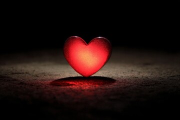 Fototapeta premium Red glowing heart shape on dark surface representing love emotion and vulnerability concept