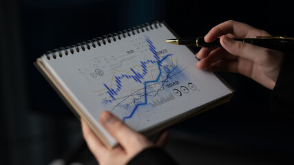 A professional analyzes financial charts and data trends in a notepad, demonstrating analytical skills and strategic planning in a modern business environment. Scalp